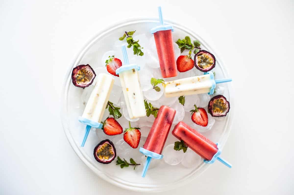 top view of pink and white popsicles on white plate with fruit