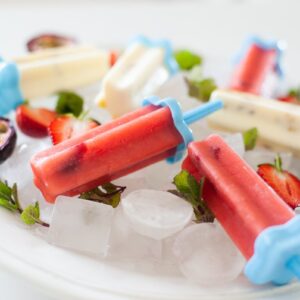 close up of pink and white fruit popsicles on white plate