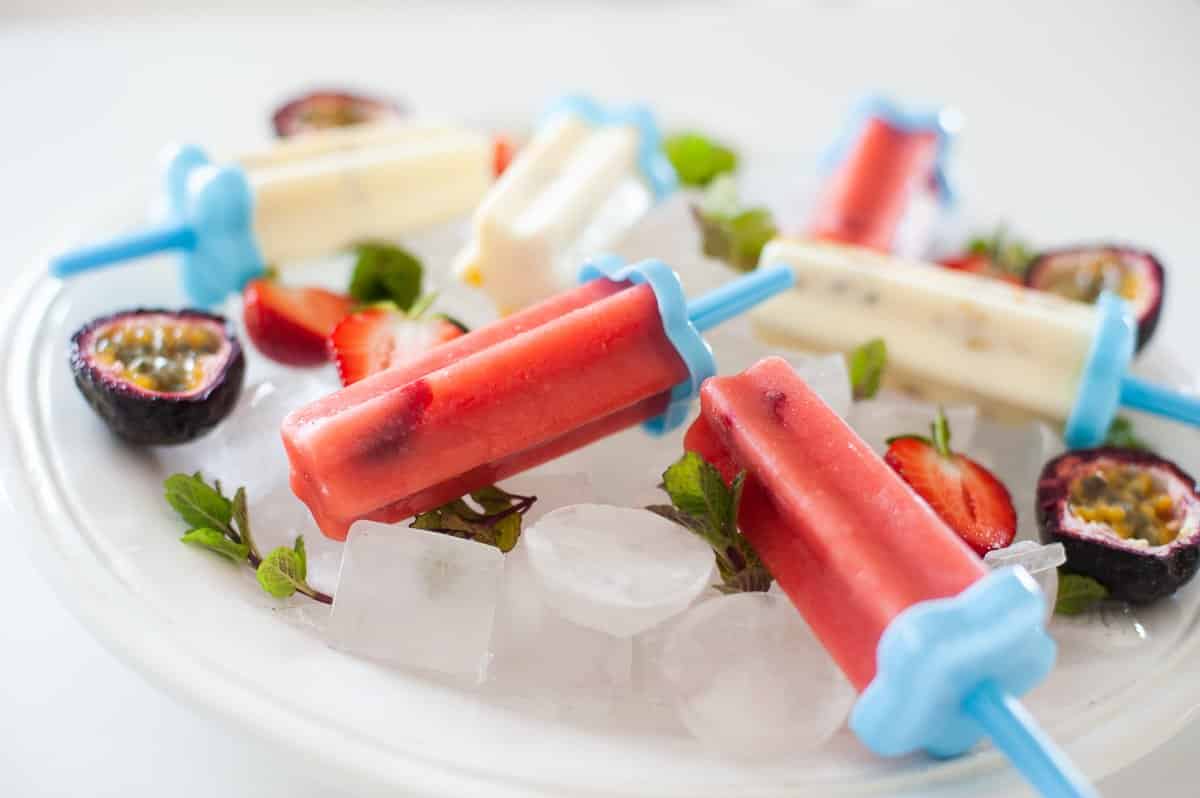 close up of pink and white fruit popsicles on white plate