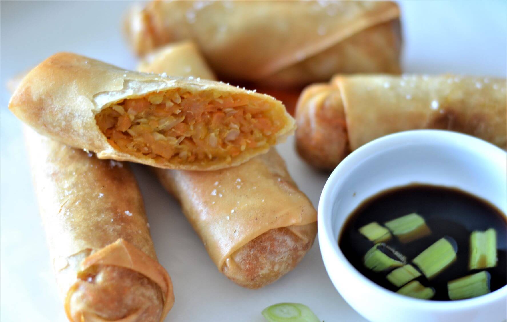 side view of sliced spring rolls with vegetable filling beside bowl of black sauce