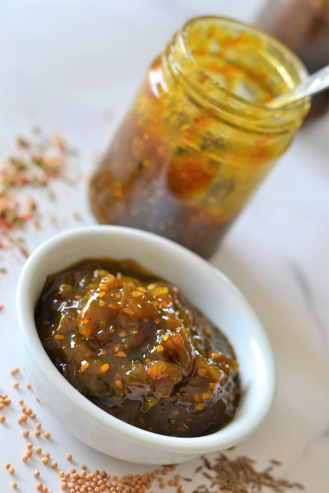 green tomato chutney in white bowl with glass jar in background