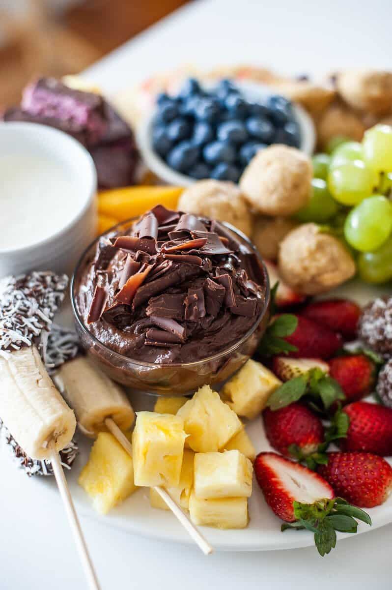 bowl of chocolate mousse on a platter, surrounded by fruit and different foods