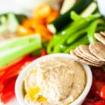 side view of hummus on a platter with chopped vegetables