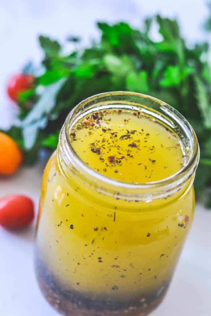 mason jar containing salad dressing with herbs in the background