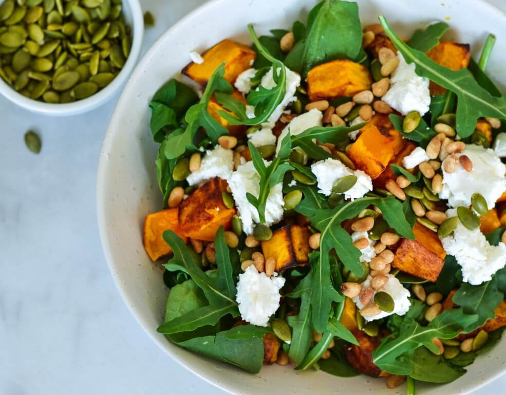 salad in a white bowl with pepitas on the side