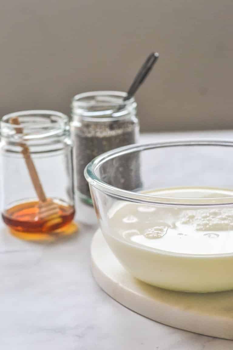 a bowl containing milk with a jars of honey and chia seeds in the background