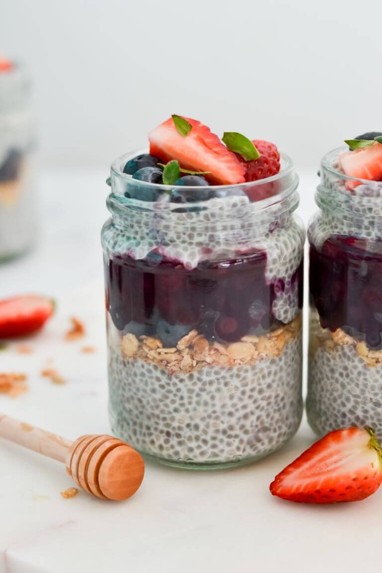 a close up of chia puddings in glass jars with honey and berries