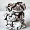 three chocolate crinkle cookies stacked on top of each other, coated in icing sugar