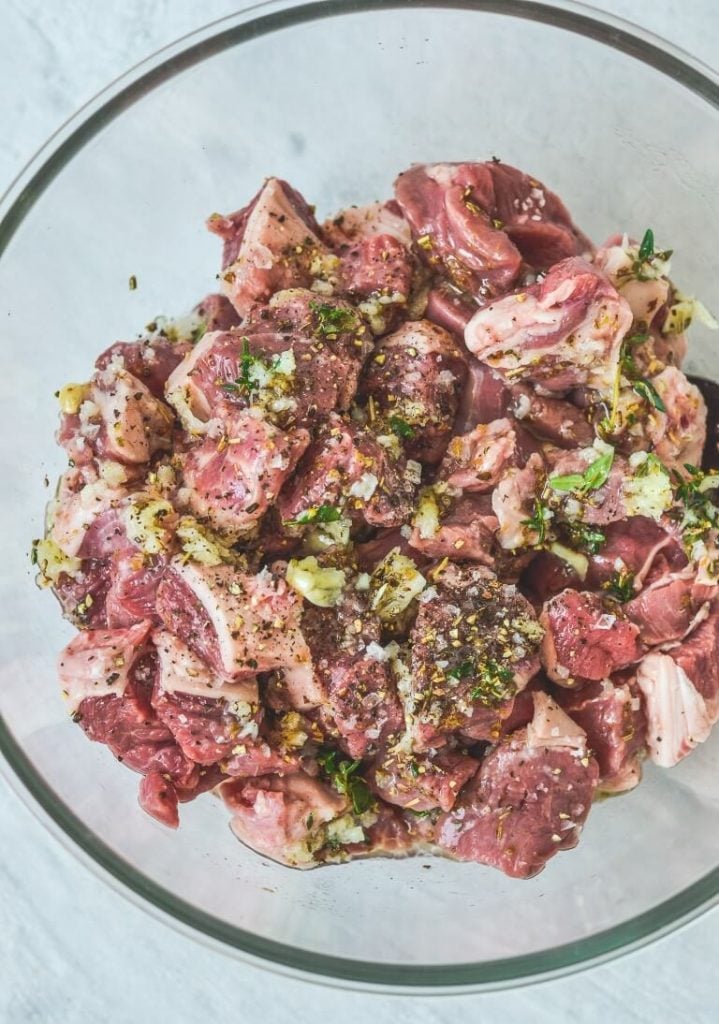 top view of a glass bowl containing lamb pieces and herbs