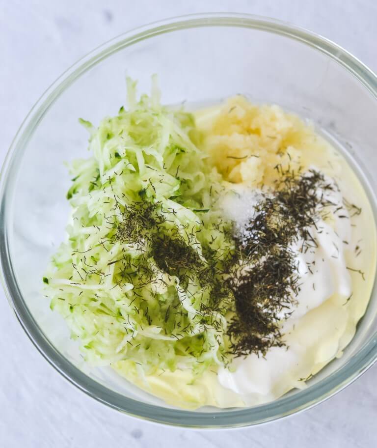 A bowl containing yoghurt, cucumber and herbs