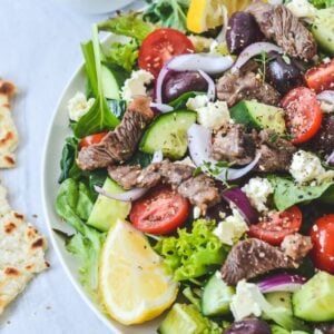 A plate of salad on a white plate, with lamb and lemon wedges