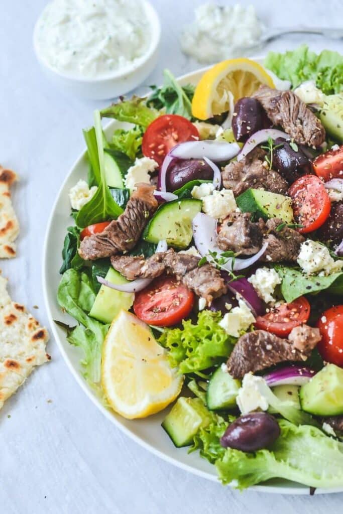 A plate of salad on a white plate, with lamb and lemon wedges