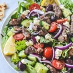 A plate of salad with olives, lamb and lemon, sprinkled with herbs