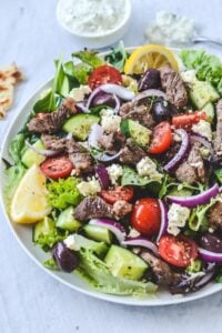 A plate of salad with olives, lamb and lemon, sprinkled with herbs