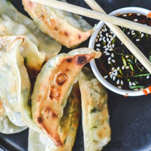 crispy gyoza on black plate with crossed chopsticks over black sauce