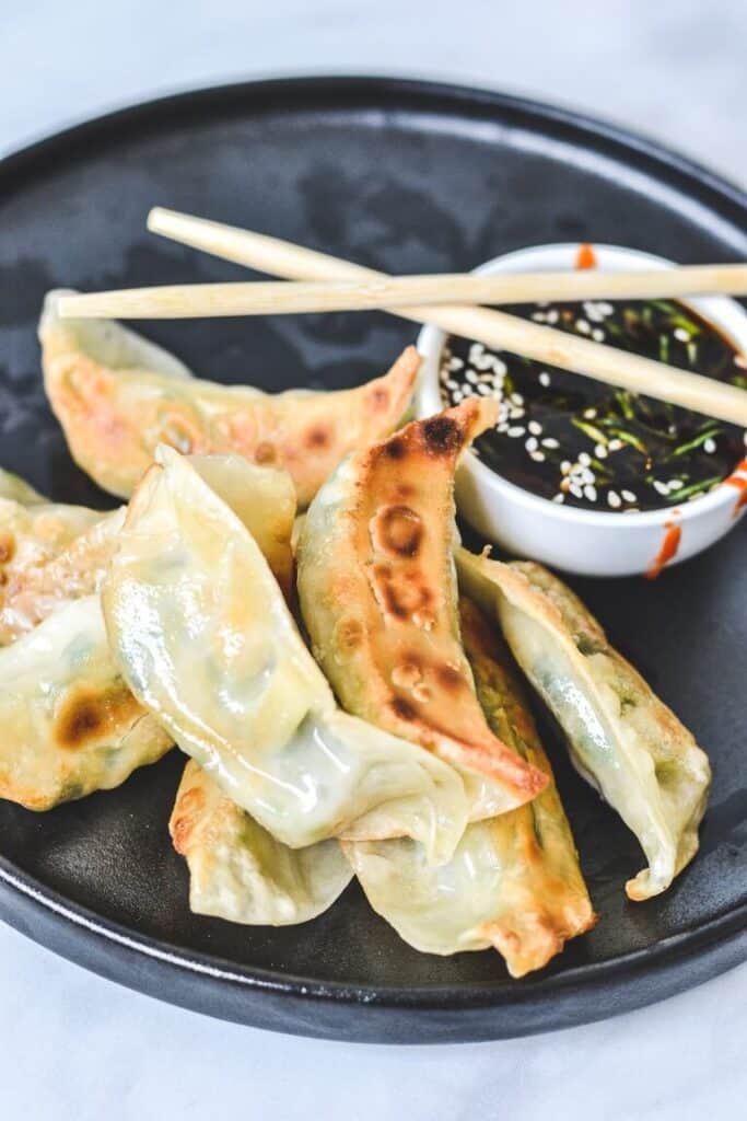 dumplings arranged on black plate with chopsticks