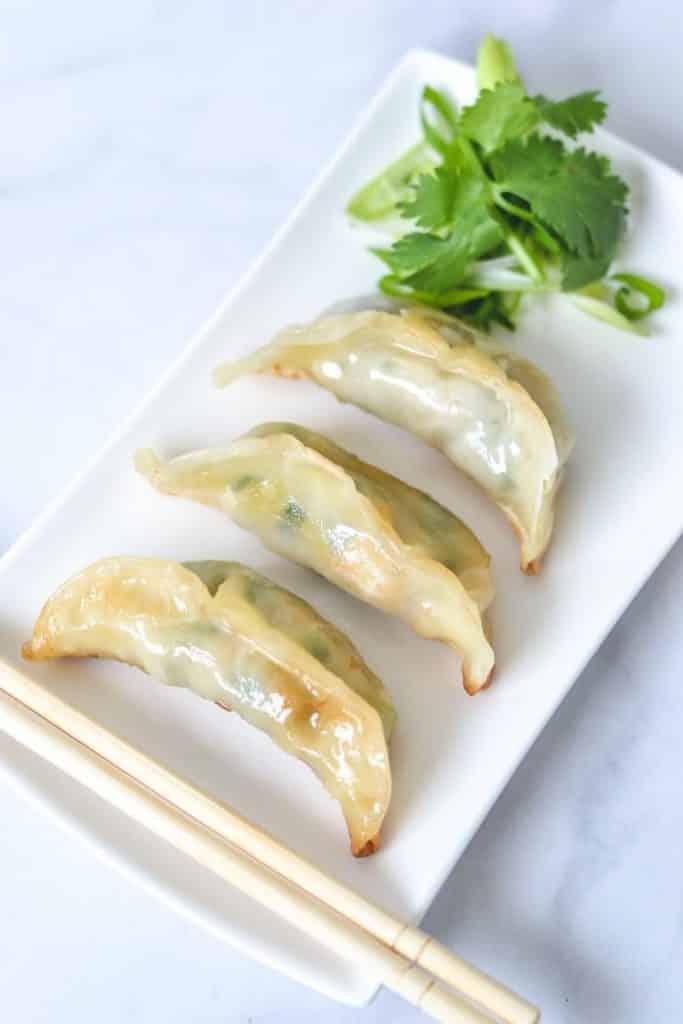 gyoza on white plate with green herbs