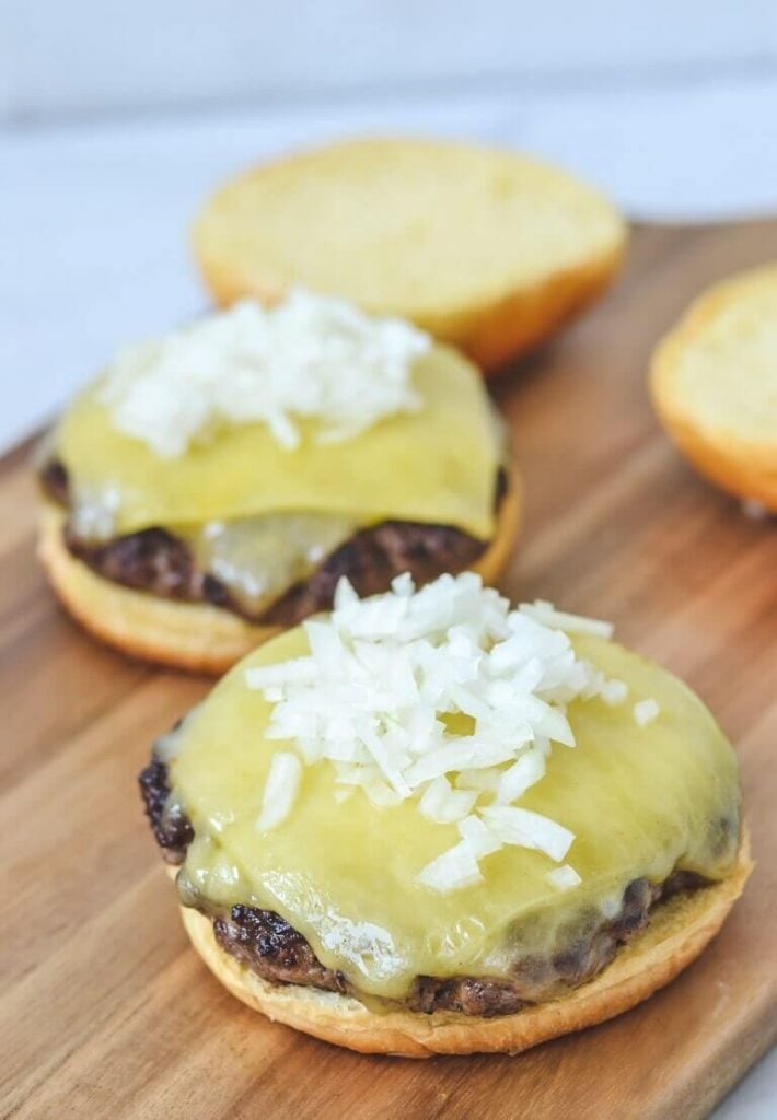 a close up of open cheeseburgers sitting on a wooden board