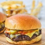 A close up of a burger with cheese and pickles on wooden board