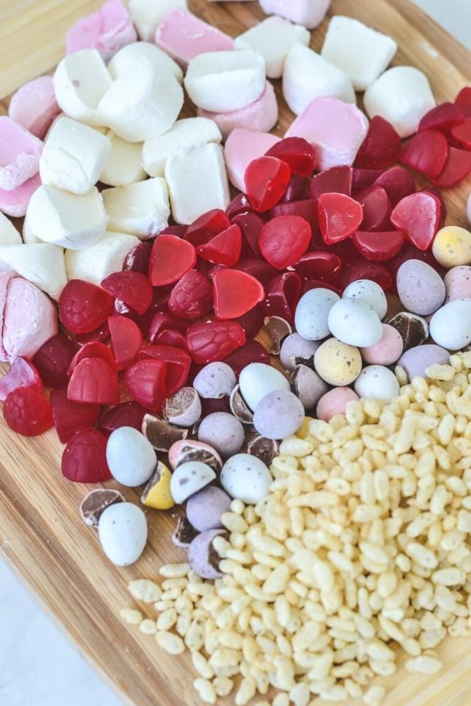 top view of marshmallows, raspberry lollies, chocolate and rice bubbles on wooden board