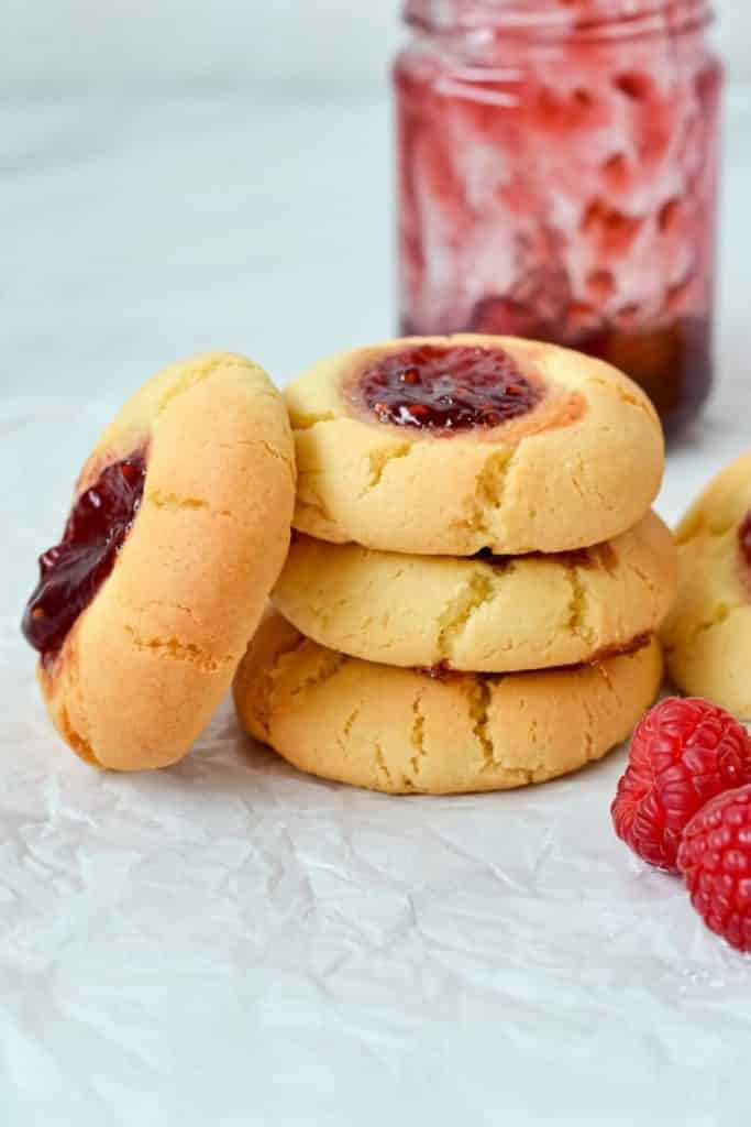 a stack of jam drop biscuits on white paper with jam and fresh raspberries