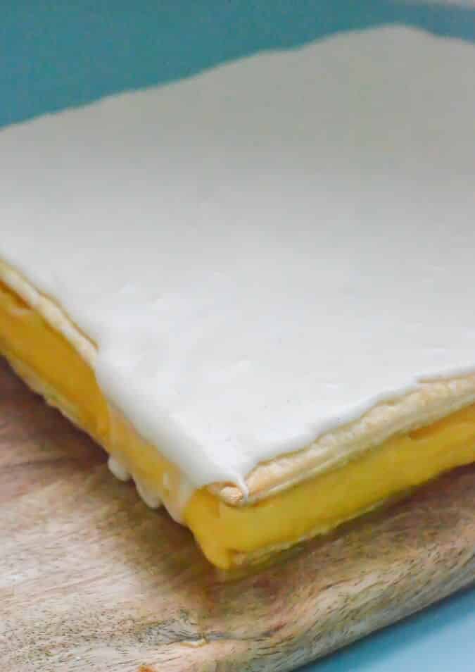 white-icing-over-finished-custard-slice-on-wooden-board