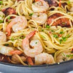 A frying pan filled with spaghetti, prawns and chorizo, sprinkled with herbs