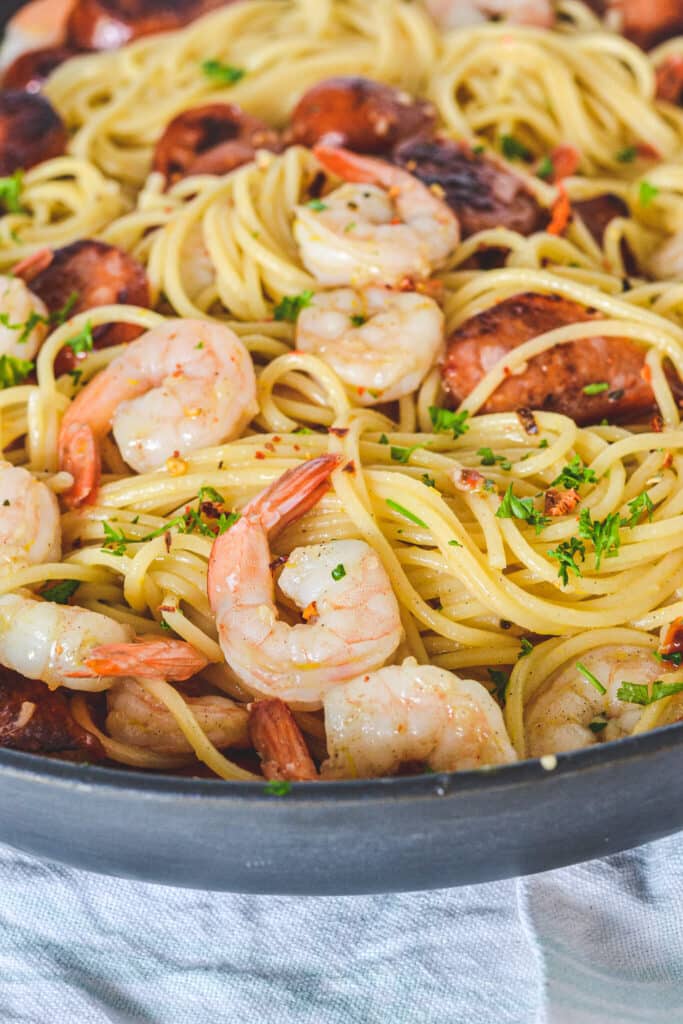 A frying pan filled with spaghetti, prawns and chorizo, sprinkled with herbs