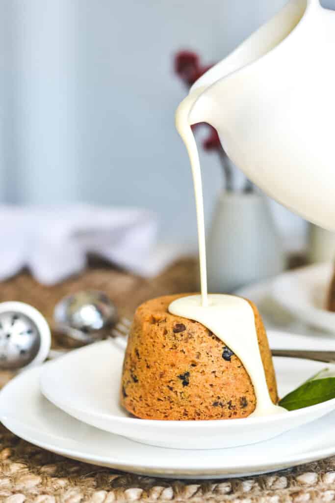 side view of a white jug pouring cream over a pudding on a white plate