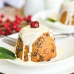 close up of a finished pudding on a white plate with cream and a cherry