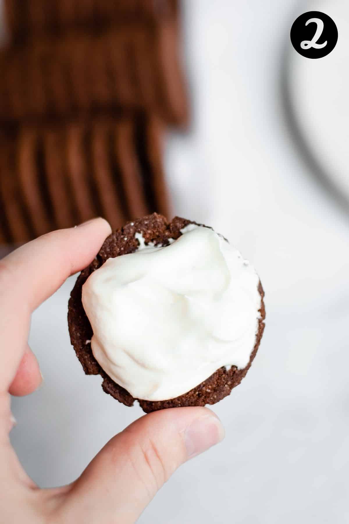 hand holding a chocolate cookie covered with cream