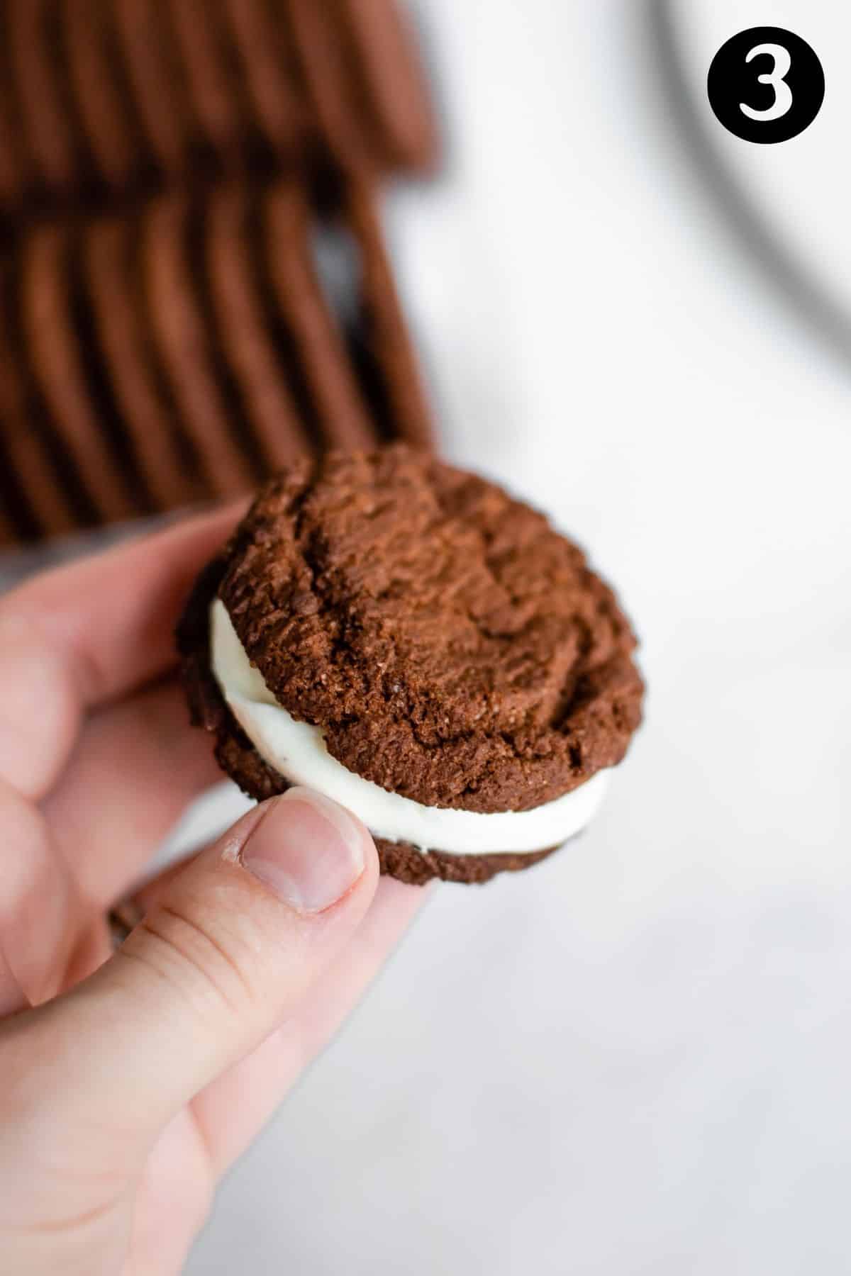 hand holding chocolate cookies with cream in the middle