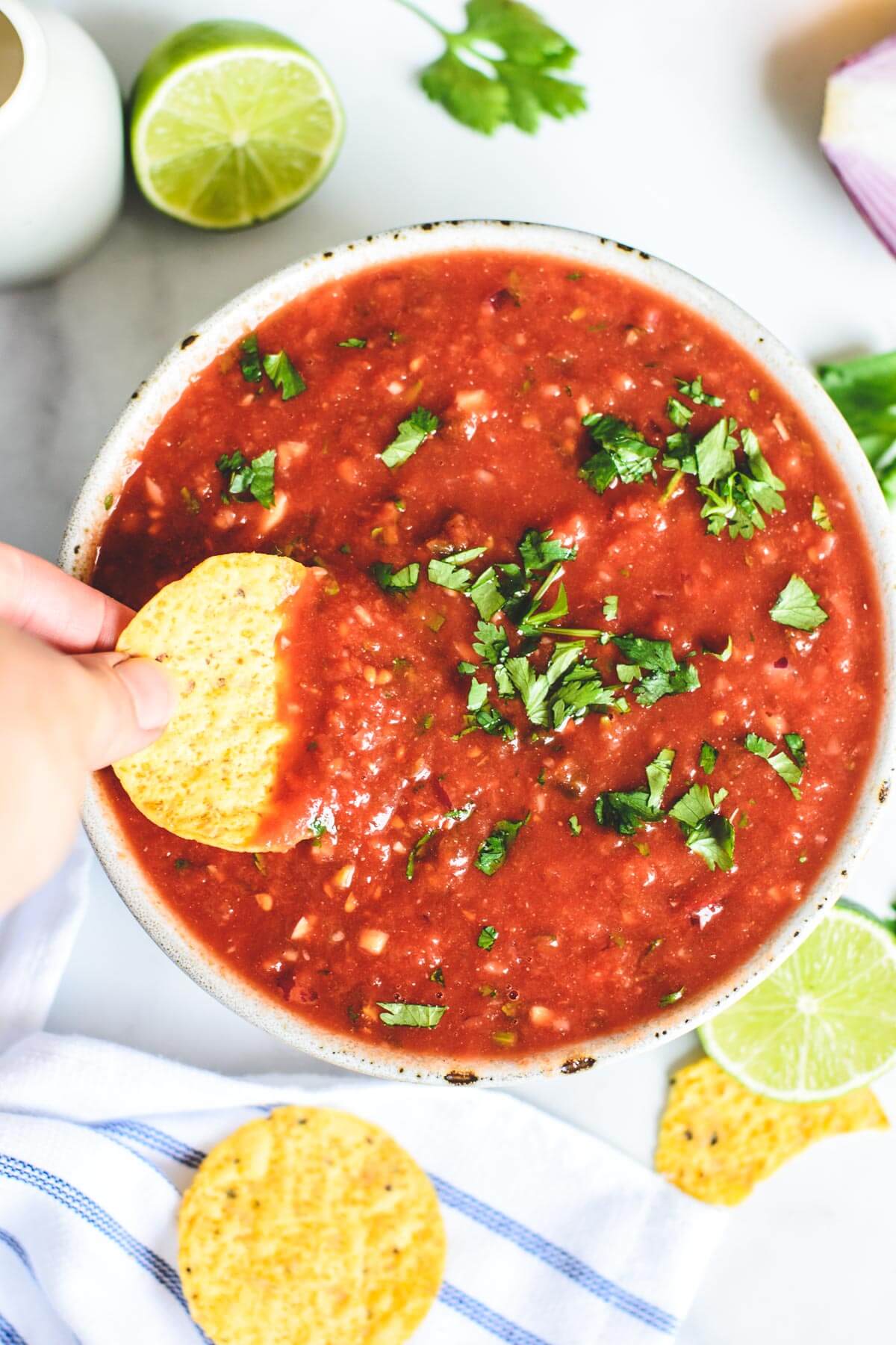 hand holding a corn chip being dipped into a bowl of red salsa
