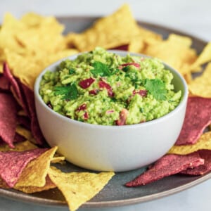 guacamole in a white bowl, surrounded by yellow and purple corn chips
