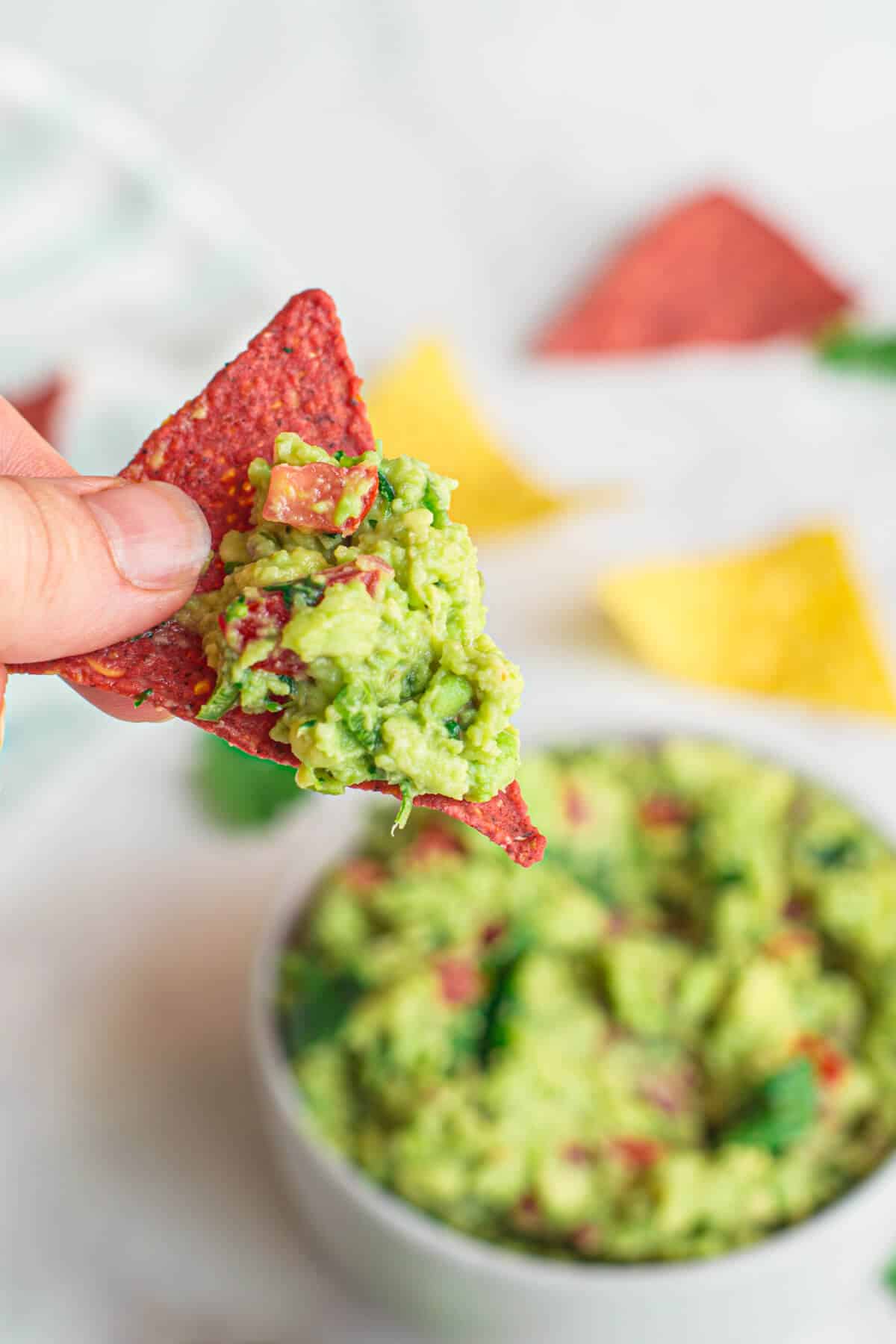 close up of a hand holding a purple corn chip with guacamole