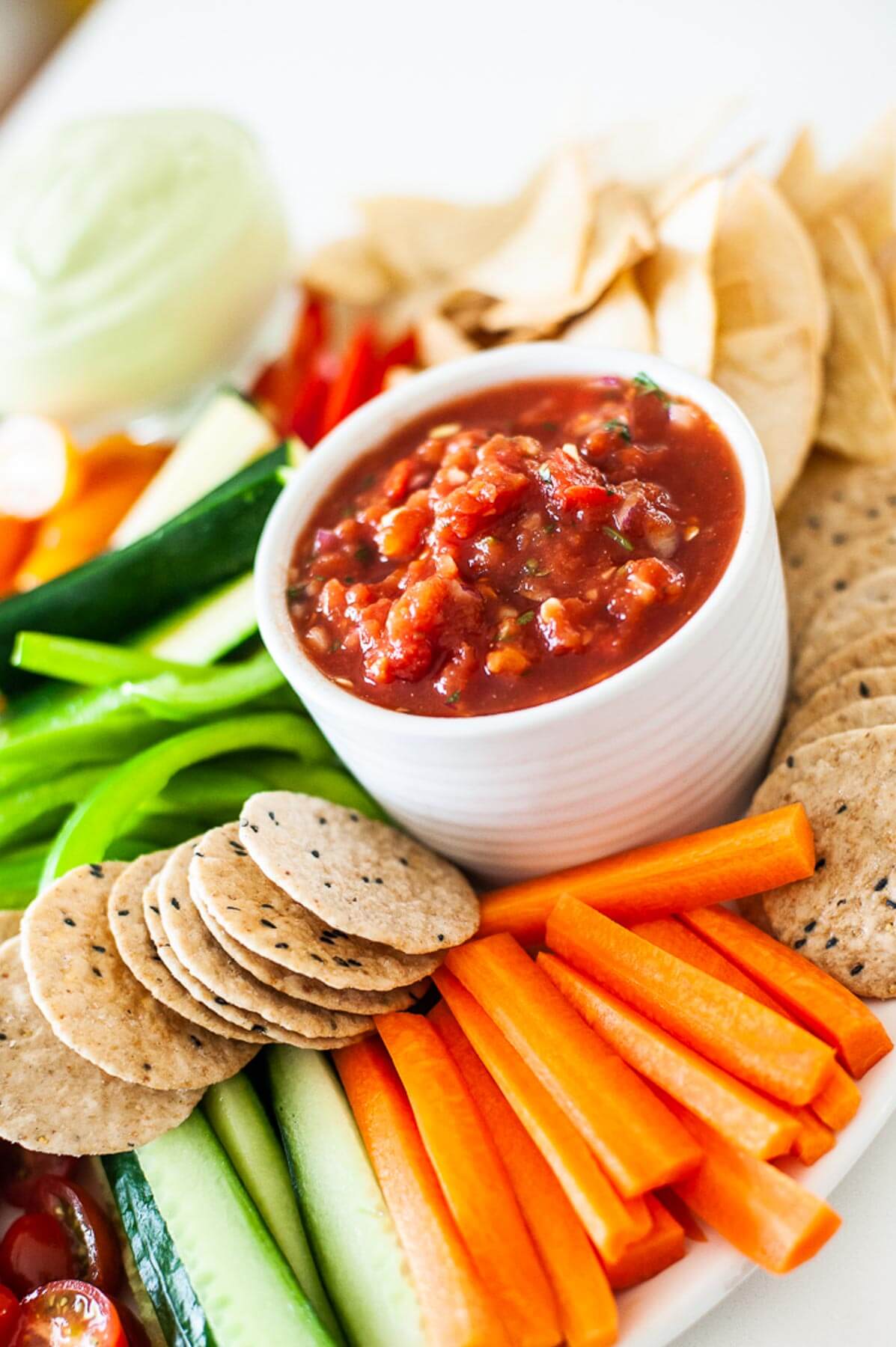 side view of a platter with sliced vegetables and salsa in a white bowl