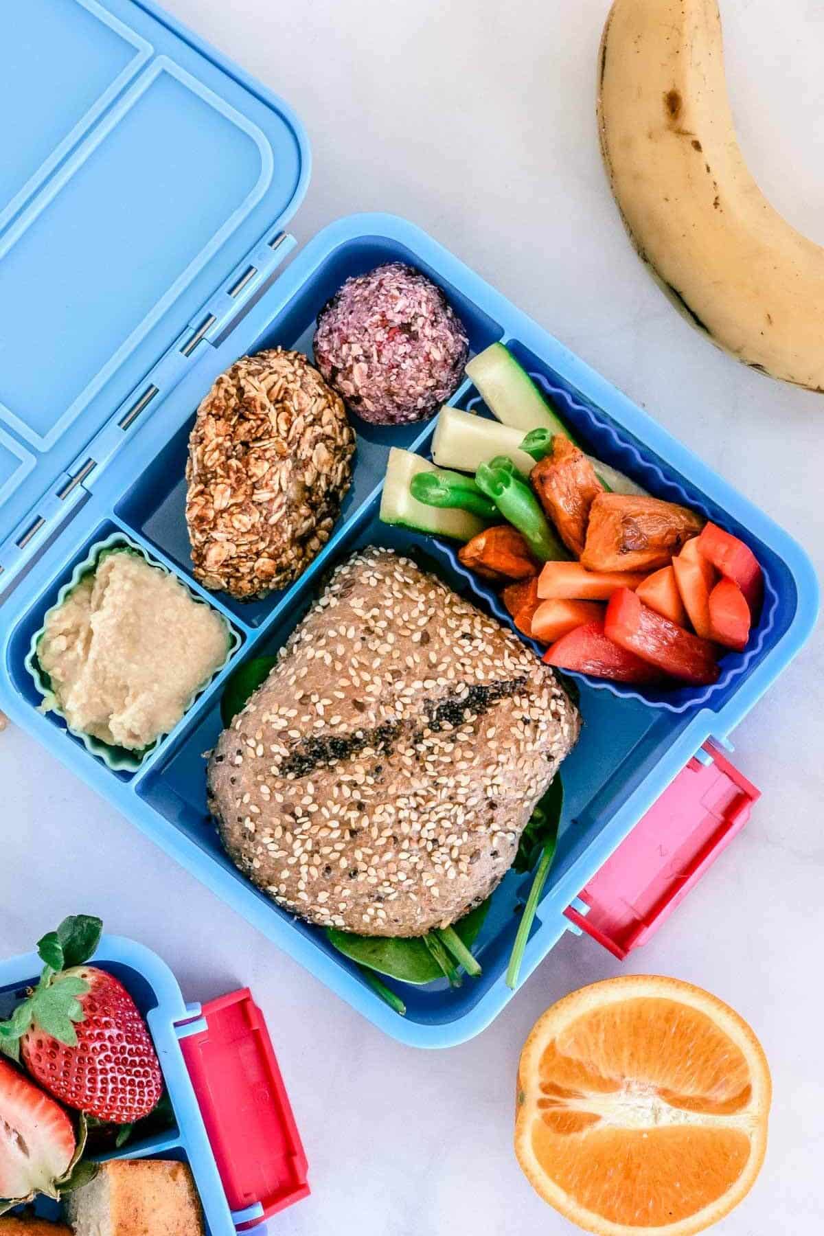 top view of a blue lunchbox with a grain roll and healthy foods