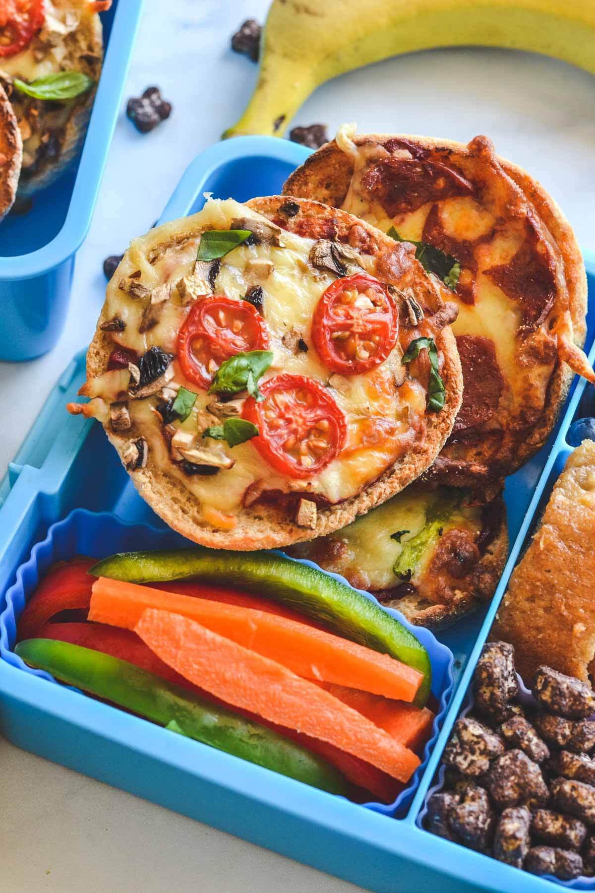 pizza muffins in a blue lunchbox with sliced vegetables