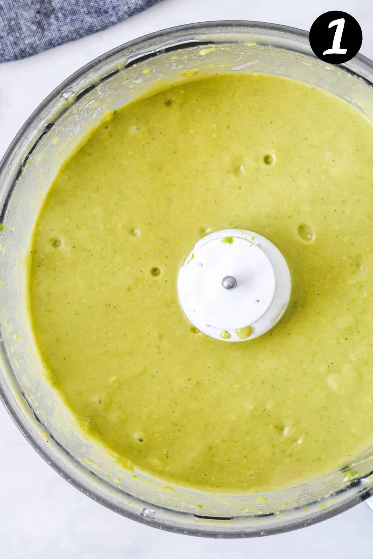 top view of avocado and wet ingredients mixed in a food processor.