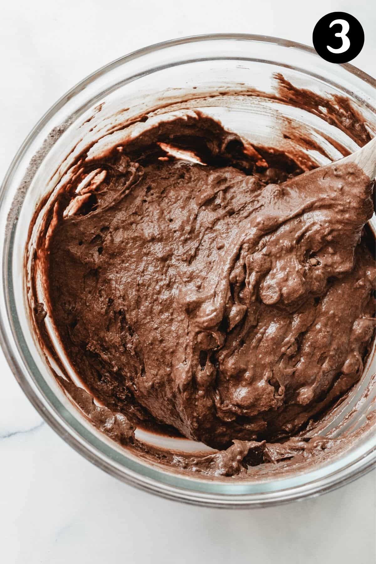 chocolate muffin batter in a glass bowl with a wooden spoon