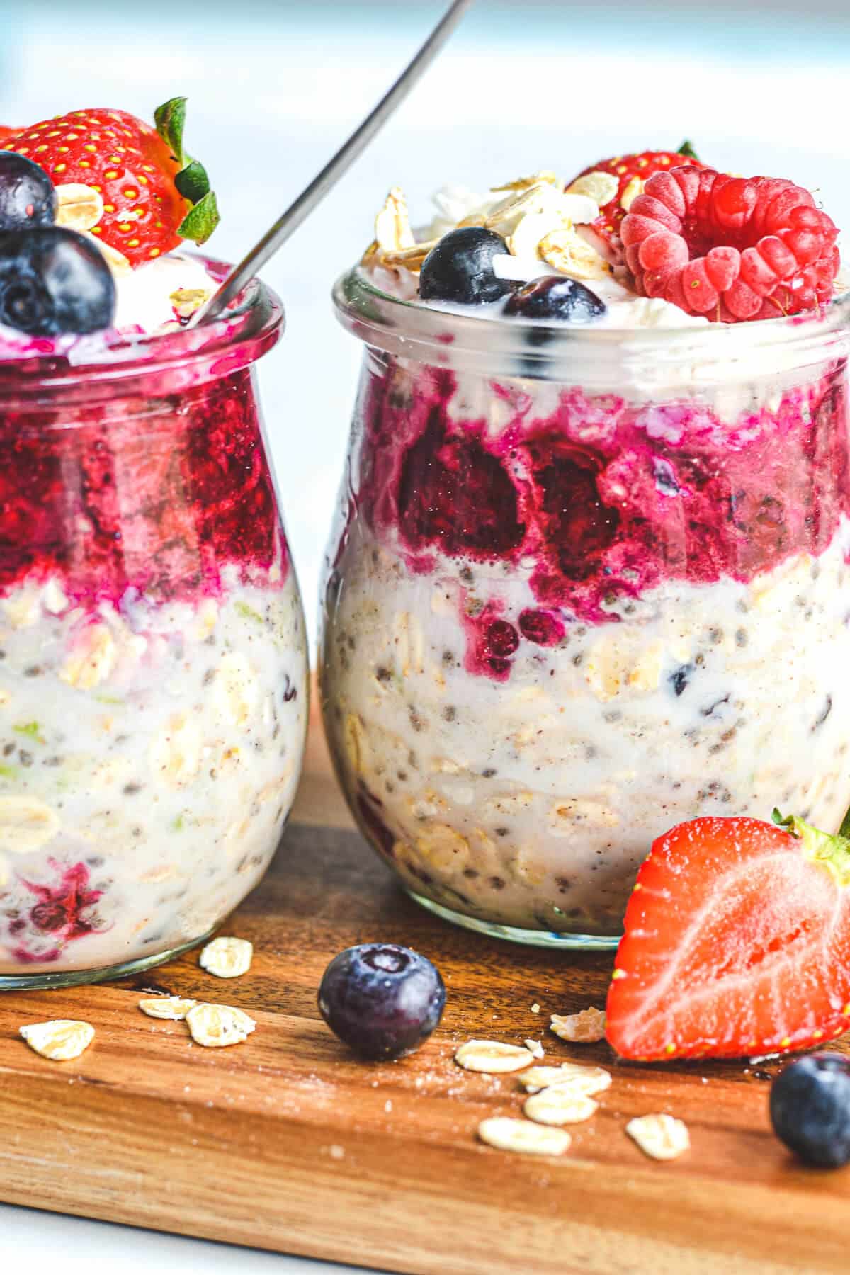 two glass jars on a wooden board containing overnight oats and topped with berries