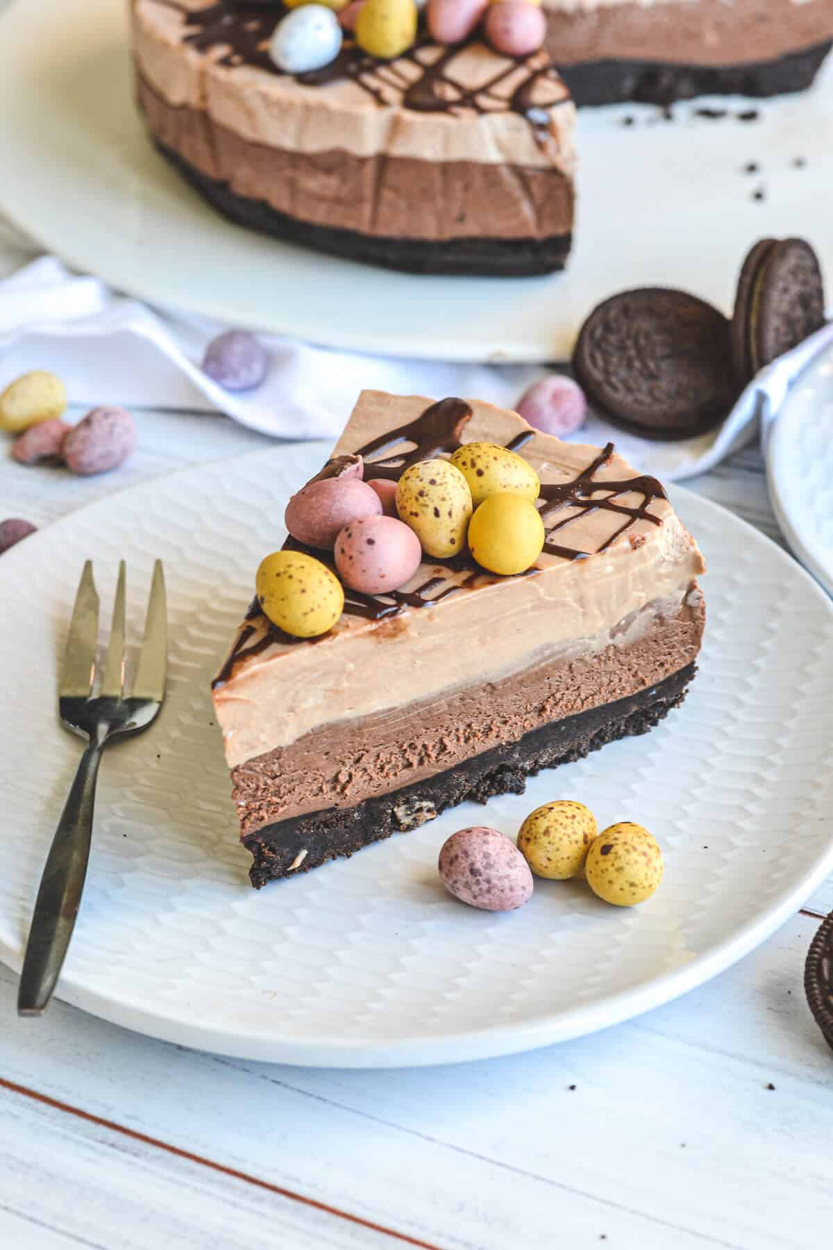 a slice of chocolate cheesecake on a white plate with mini Easter eggs