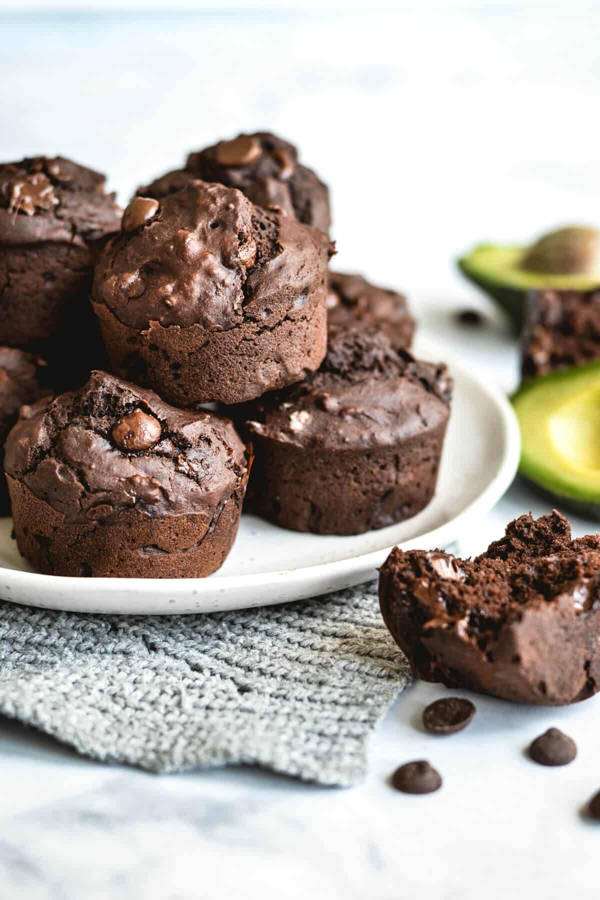 finished muffins on a white plate with avocados and chocolate chips on a white bench