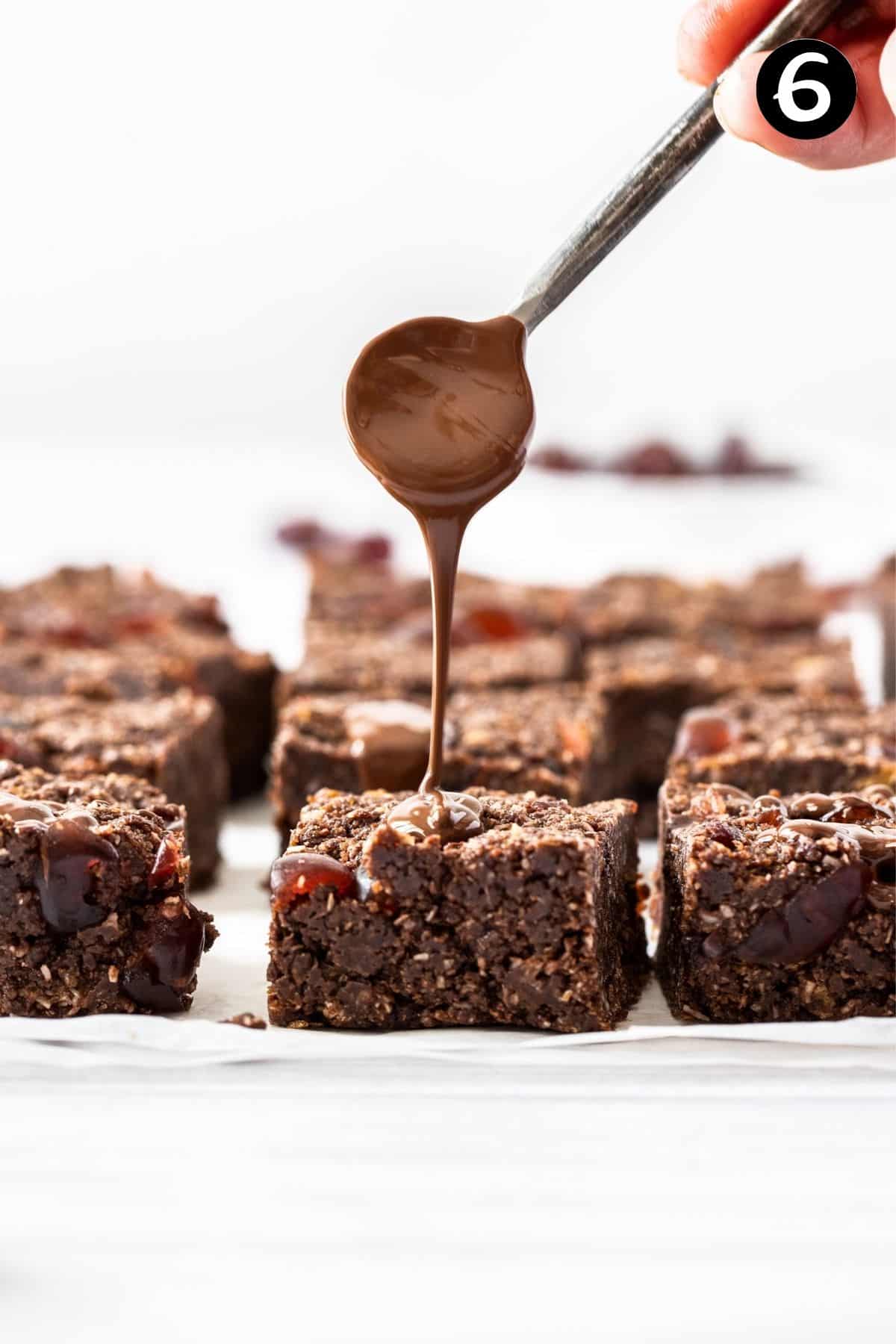 a spoon drizzling melted chocolate over pieces of chocolate slice