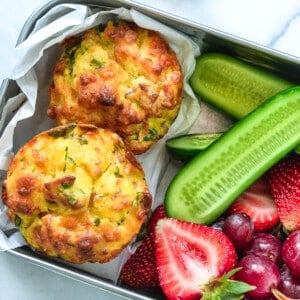 close up of a lunchbox containing savoury muffins, fruit and cucumber