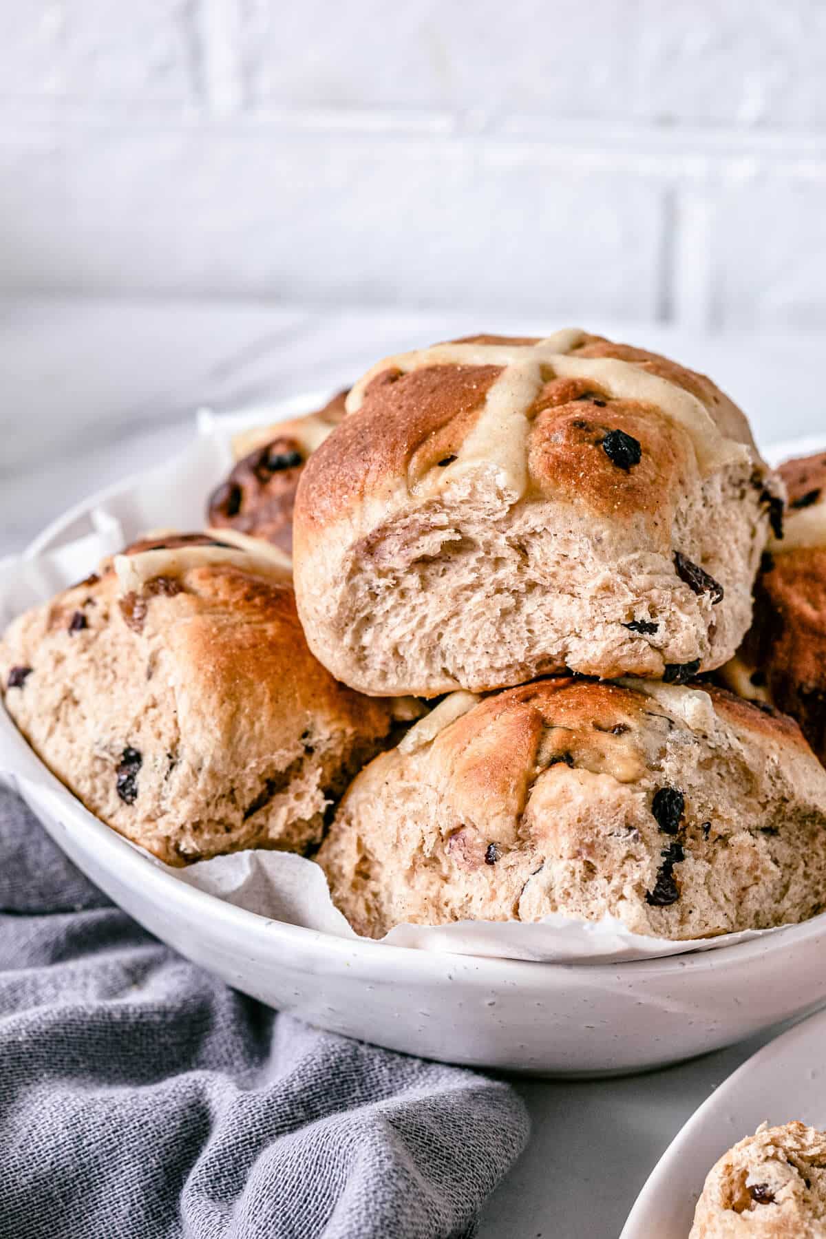 a white bowl containing hot cross buns on a white bench