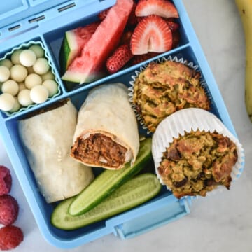 top view of a blue bento lunchbox containing muffins and healthy foods