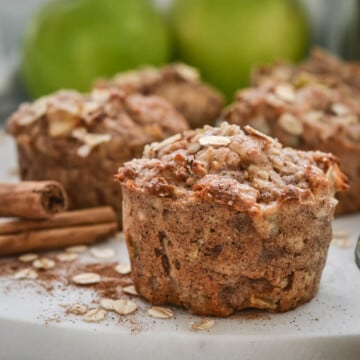close up of an apple muffin on a white plate with cinnamon sticks
