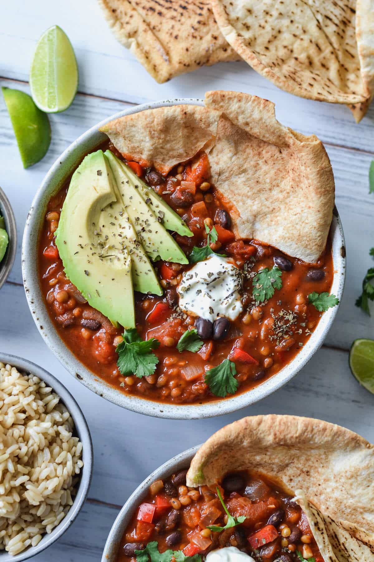 top view of chilli sin carne in a grey bowl with sliced avocado and pita bread