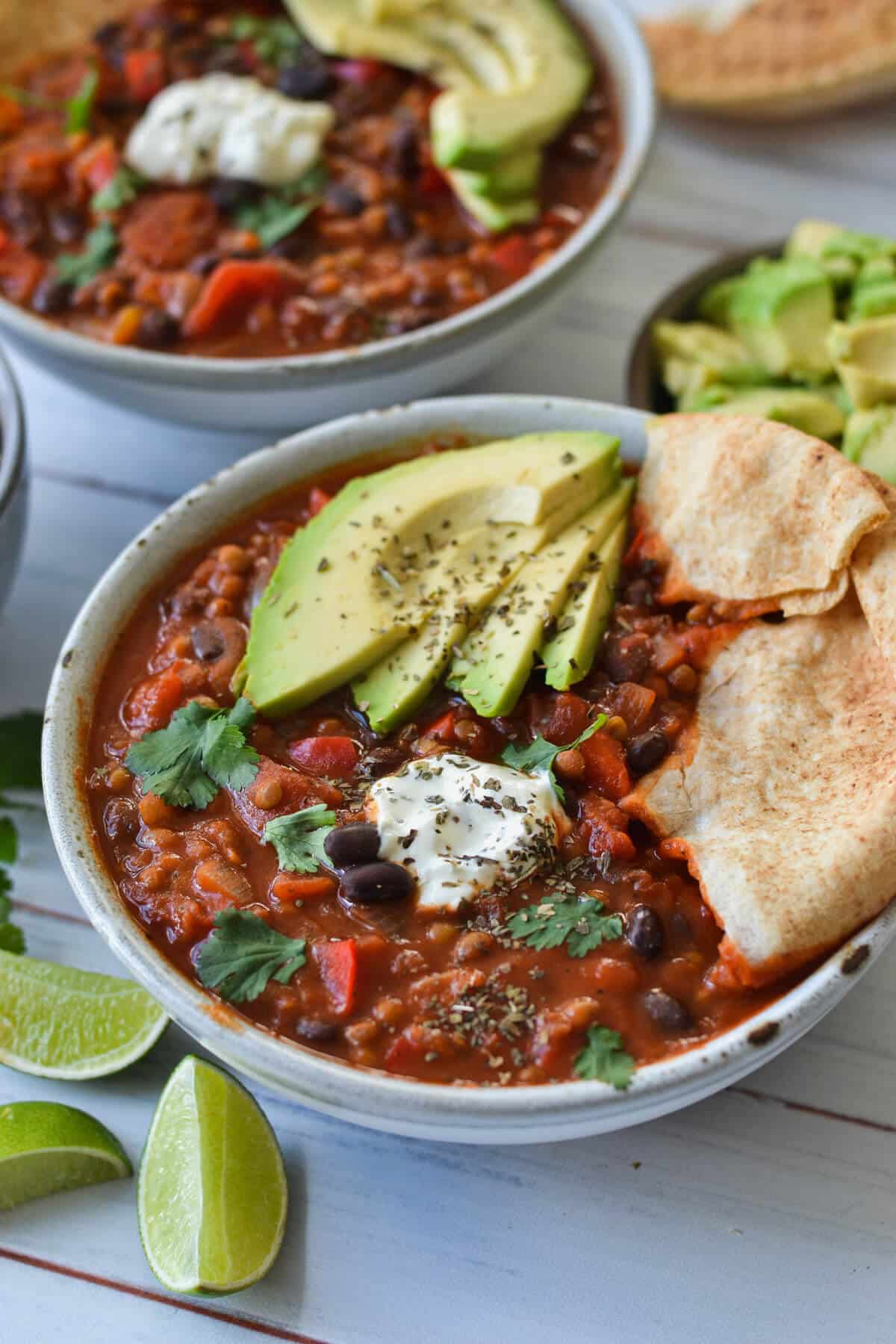 side view of vegetarian chilli in a grey bowl topped with pita bread and avocado.